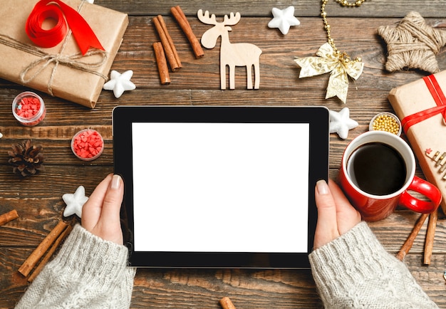 Vrouwelijke handen maakt gebruik van een tablet, zittend aan een tafel met kerstaccessoires