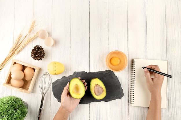 Vrouwelijke handen maken aantekeningen in dieet boek, bovenaanzicht, concept, kopie ruimte, hand met avocado