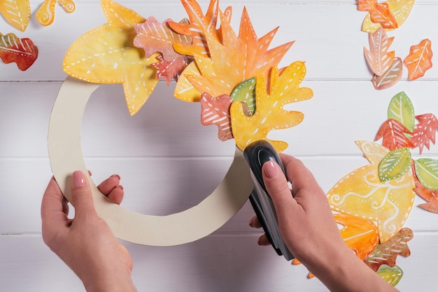 Vrouwelijke handen maken decoratieve herfstpapieren krans Met behulp van nietmachine om bladeren in cirkel op kartonnen vorm bovenaanzicht te bevestigen