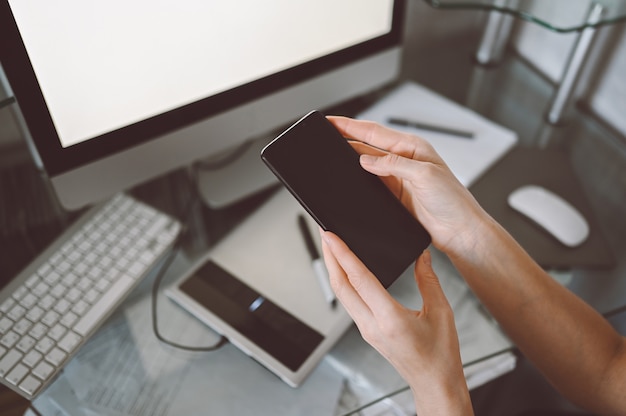 Vrouwelijke handen met behulp van slimme telefoon in interieur werkplek, freelance zakenvrouw met behulp van mobiele telefoon op kantoor, werken vanuit huis met behulp van slimme telefoon en notebook computer. Quarantaine op afstand