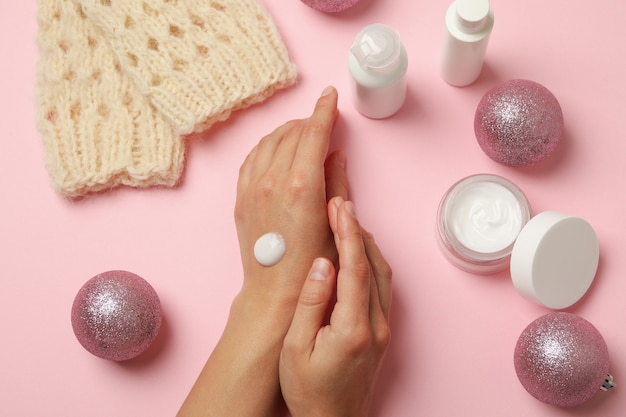 Vrouwelijke handen met cosmetische crème op roze achtergrond met kerstaccessoires