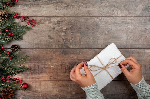 Vrouwelijke handen met de doos van de gift van Kerstmis op donkere houten achtergrond met dennentakken
