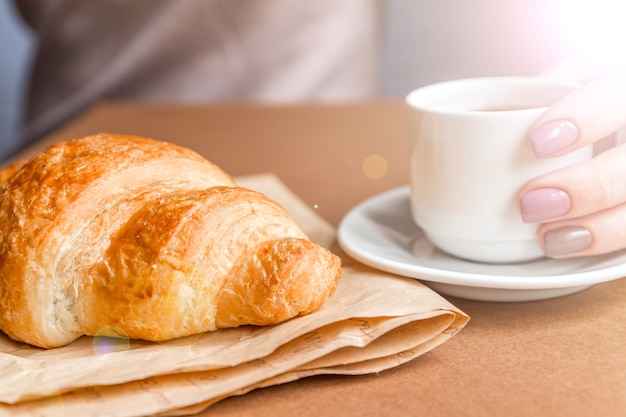 Vrouwelijke handen met de kop van de manicureholding van koffie en het eten van croissant. Ontbijt in Franse stijl