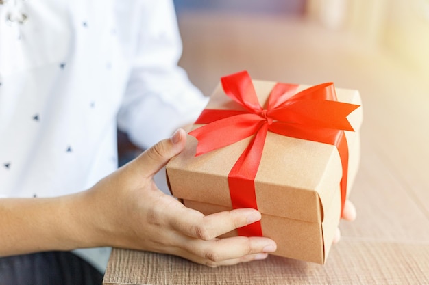 Vrouwelijke handen met een geschenk omwikkeld met rood lint