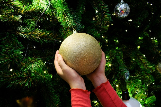 Vrouwelijke handen met een gouden bal. Gedecoreerde kerstboom in zilver en goud thema.