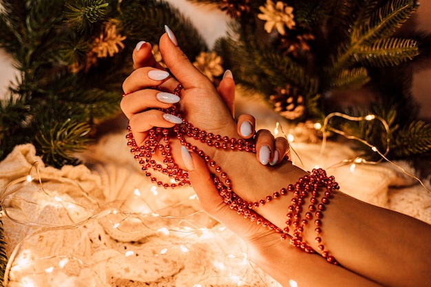 Vrouwelijke handen met een kerstslinger van rode kralen op een achtergrond van pijnboomtakken