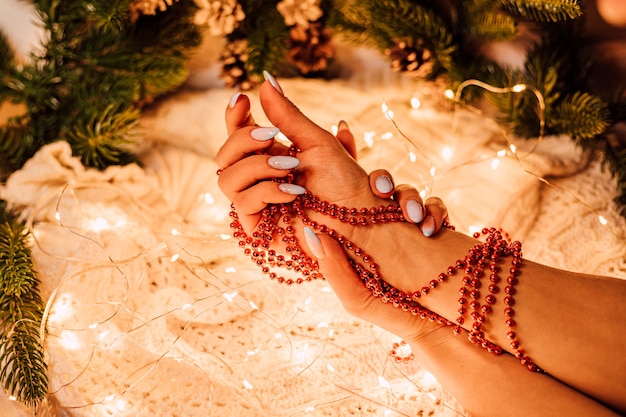 Vrouwelijke handen met een kerstslinger van rode kralen op een achtergrond van pijnboomtakken