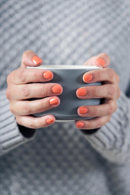 Vrouwelijke handen met een kopje koffie met grijze gebreide trui Koffie in de ochtend