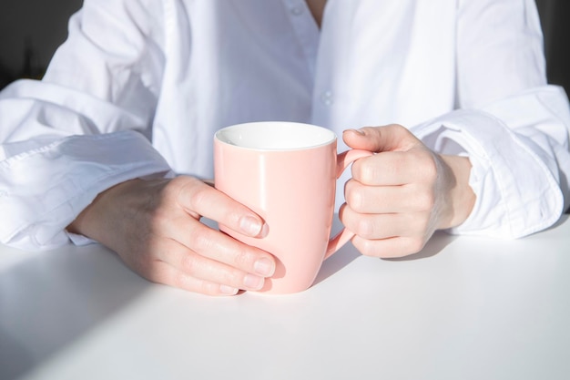 Vrouwelijke handen met een kopje koffie op een witte tafel onder de ochtendzon