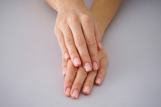 Vrouwelijke handen met een mooie manicure op een grijze achtergrond.