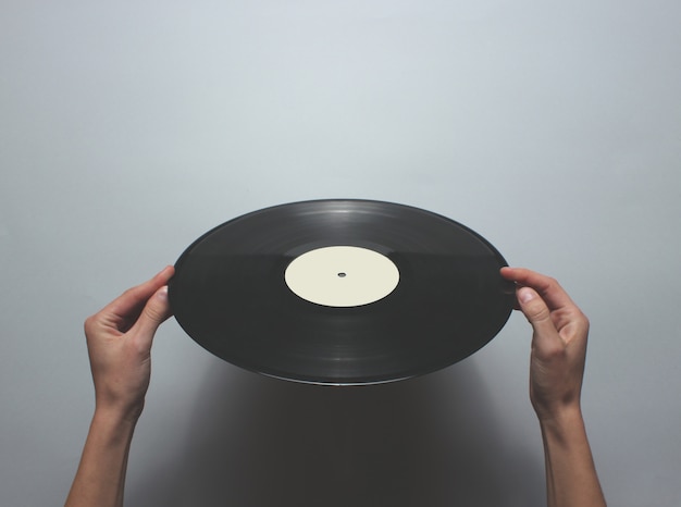 Vrouwelijke handen met een retro vinyl record op een grijze tafel. Bovenaanzicht, minimalisme.