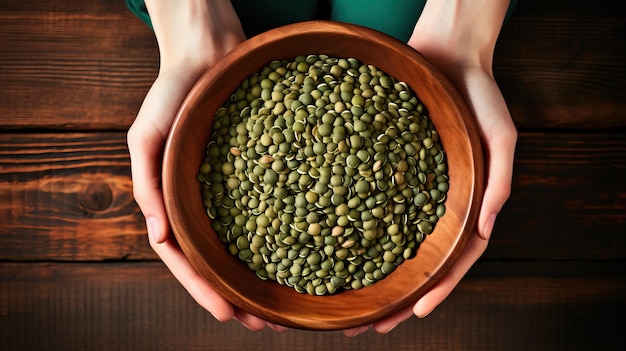 Vrouwelijke handen met een schaal met groene linzen op een houten tafel