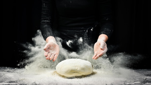 Vrouwelijke handen met een stuk deeg voor het bakken van brood Zwarte kookachtergrond