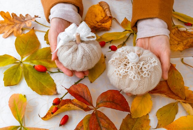 Vrouwelijke handen met gebreide pompoenen met gele herfstbladeren