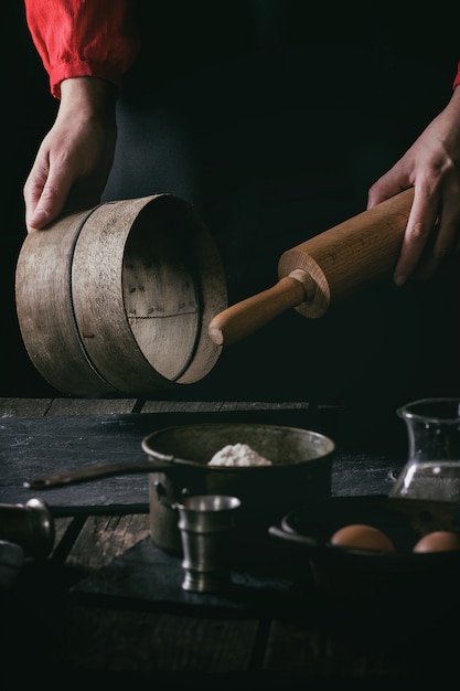 Vrouwelijke handen met houten deegrol en zeef