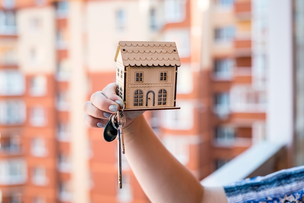Vrouwelijke handen met houten huismodel en sleutels
