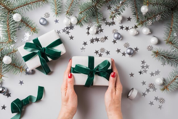 Vrouwelijke handen met kerstcadeau doos met groen fluwelen lint met dennentakken, zilveren ballen. Kerstmis en gelukkig nieuwjaarskaart. Plat lag, bovenaanzicht