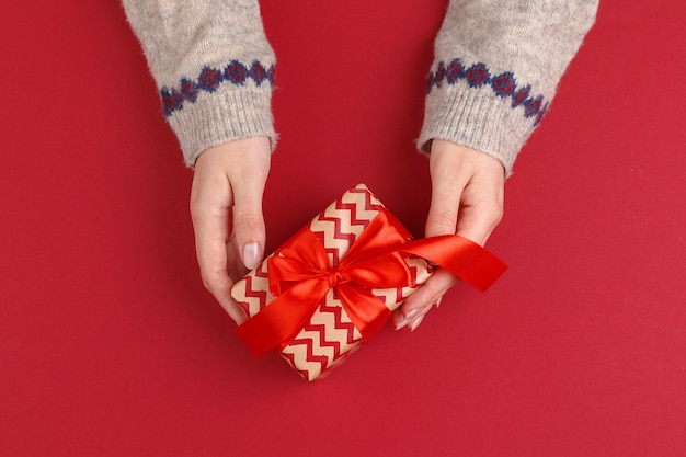 Vrouwelijke handen met kerstcadeau op rode achtergrond bovenaanzicht kopie ruimte