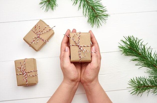 Vrouwelijke handen met kerstcadeaudozen boven witte tafel met pijnboomtakken