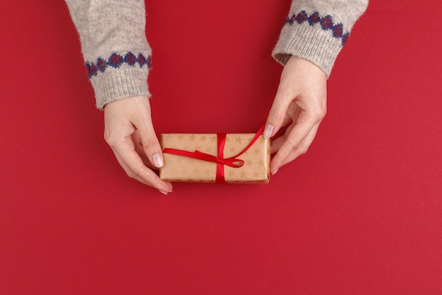 Vrouwelijke handen met Kerstmisgift op rode achtergrond, hoogste mening, exemplaarruimte