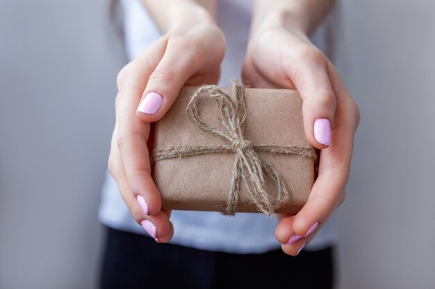 Vrouwelijke handen met kleine geschenkdoos verpakt ambachtelijk papier met lint. Klein kerst- of nieuwjaarsgeschenk in de handen van een vrouw. Kerst verjaardag valentijn viering aanwezig romantisch concept