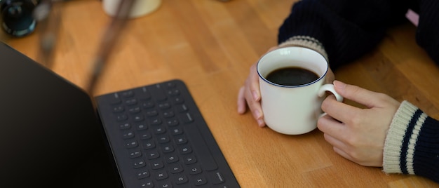 Vrouwelijke handen met koffiekopje op houten werktafel met digitale tablet en decoratie