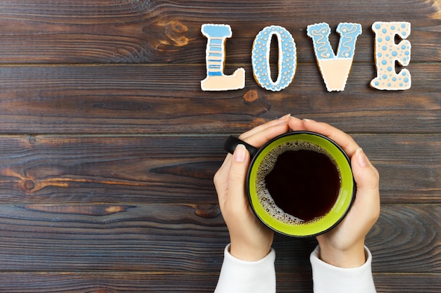 Vrouwelijke handen met kopje koffie en koekjes op houten tafel