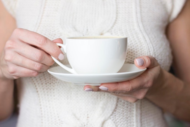 Vrouwelijke handen met kopje koffie of thee. Vrouw in gebreide trui. Winter ontspannen.