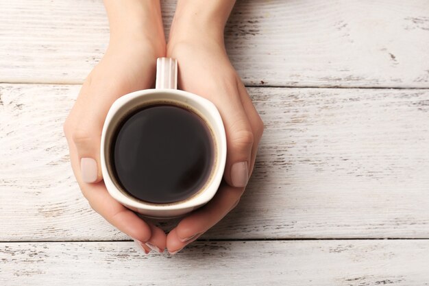 Vrouwelijke handen met kopje koffie op houten