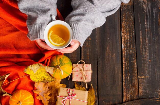 Foto vrouwelijke handen met kopje thee met citroen op houten tafel met herfstbladeren, pompoenen