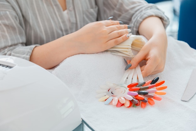 Vrouwelijke handen met kunstmatige acrylnagels pikken nieuwe nagellakkleur op tijdens de manicureprocedure. Gekleurd nagellakproces op manicure in schoonheidssalon. Hygiëne en schoonheid van handen in nagelsalon.