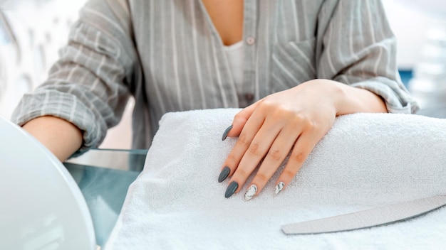 Vrouwelijke handen met kunstmatige acrylnagels tijdens manicure procedure gekleurde nagellak op manicure in schoonheidssalon client droogt nagels in lamp in salon hygiëne en schoonheid van handen lange webbanner