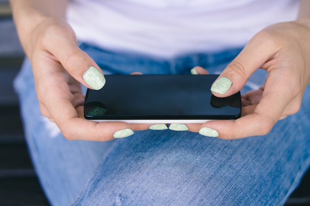 Vrouwelijke handen met manicure die een mobiele telefoon in openlucht dicht tegenhouden