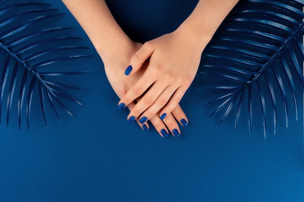 Vrouwelijke handen met manicure van klassieke blauwe kleur met bladeren