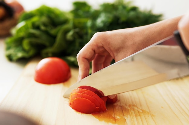 Vrouwelijke handen met mes snijden rode tomaat op houten snijplank