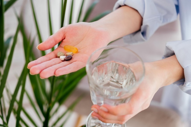 Foto vrouwelijke handen met pillen, vitamines, capsules en glas water voor bladeren binnenshuis