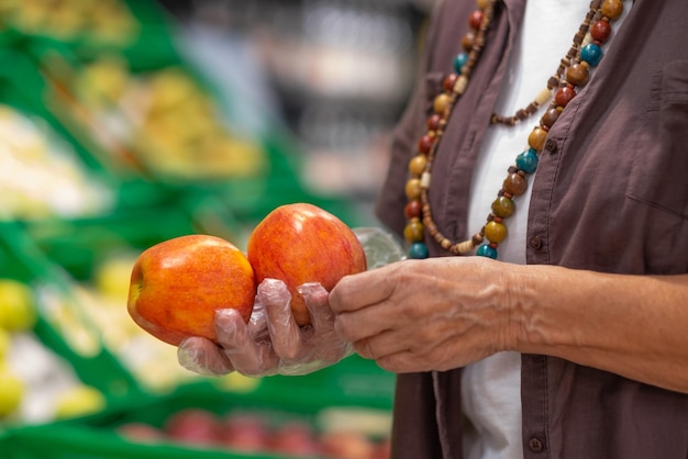 Vrouwelijke handen met rode appels in een supermarkt of supermarkt close-up Vrouw houdt twee appels fruit met beschermende handschoenen