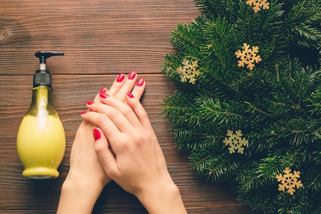 Vrouwelijke handen met rode manicure en een fles handcrème op een houten tafel