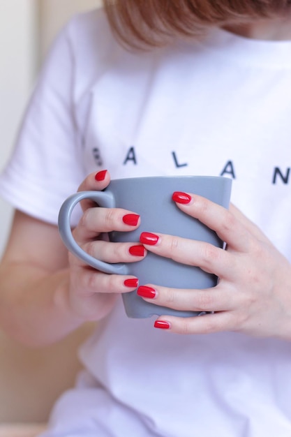 Vrouwelijke handen met rode manicure houden een mok wit T-shirt met inscriptie balans