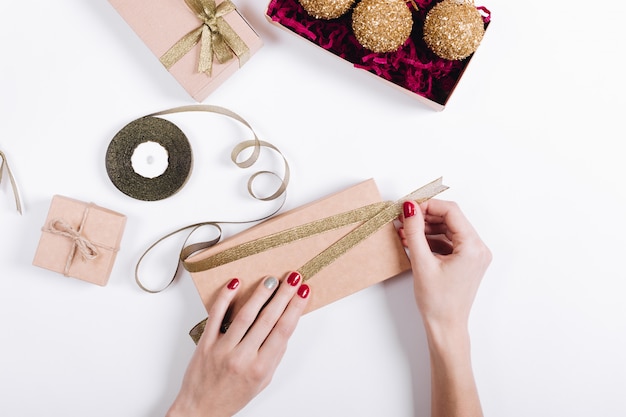 Vrouwelijke handen met rode manicure pakken de geschenken in dozen in en binden ze met linten