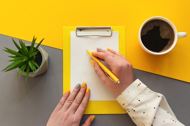 Vrouwelijke handen met schrijven op papier Werkplek met klembord kopje koffie en vetplant