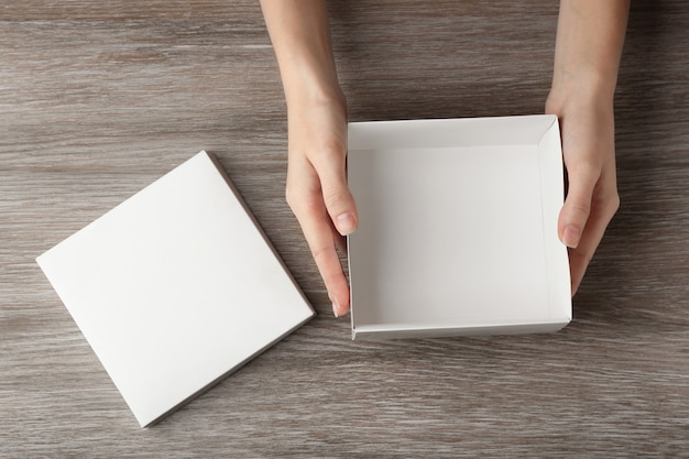 Vrouwelijke handen met witte open doos op houten oppervlak