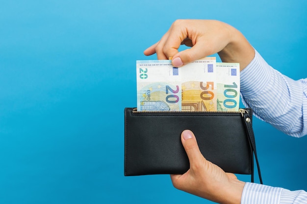Vrouwelijke handen met zwarte portemonnee met eurobankbiljetten op een blauwe achtergrond