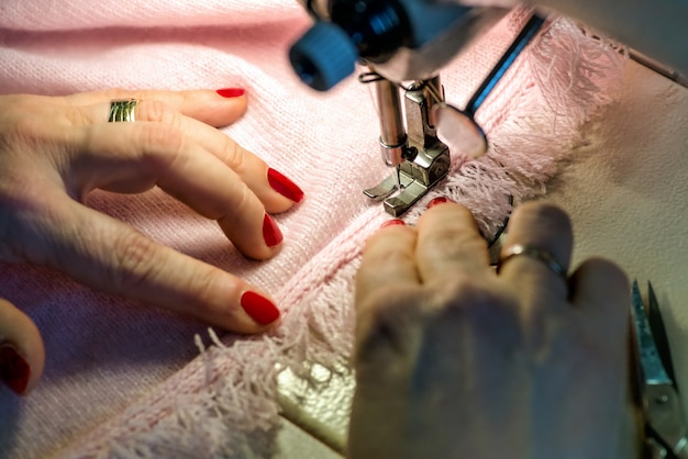 Vrouwelijke handen naaien Fringe op roze kledingstuk