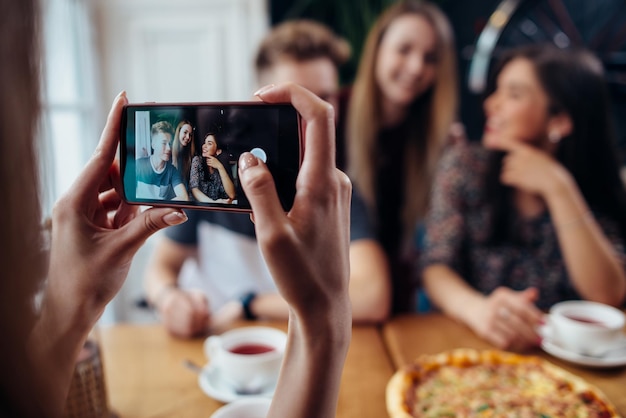 Vrouwelijke handen nemen foto met smartphone van jonge vrolijke vrienden wazig achtergrond