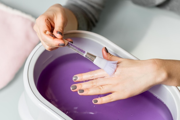 Vrouwelijke handen nemen procedure in een lila paraffinekom. Cosmetologische en huidverzorging apparatuur in een beauty & spa salon.