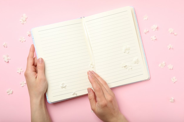 Vrouwelijke handen, notebook en hortensia bloemblaadjes op roze ruimte