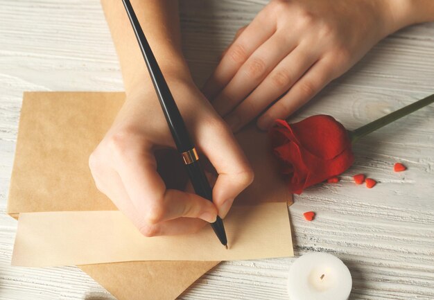 Vrouwelijke handen ondertekenen cadeaubon voor Valentijnsdag op witte houten achtergrond