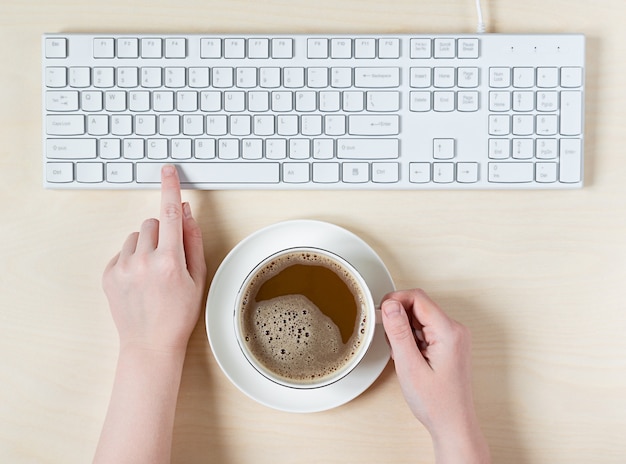Vrouwelijke handen op het toetsenbord en kopje koffie te houden.