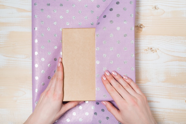 Vrouwelijke handen pakken een geschenk in een glanzend violet polka-dot papier, bovenaanzicht